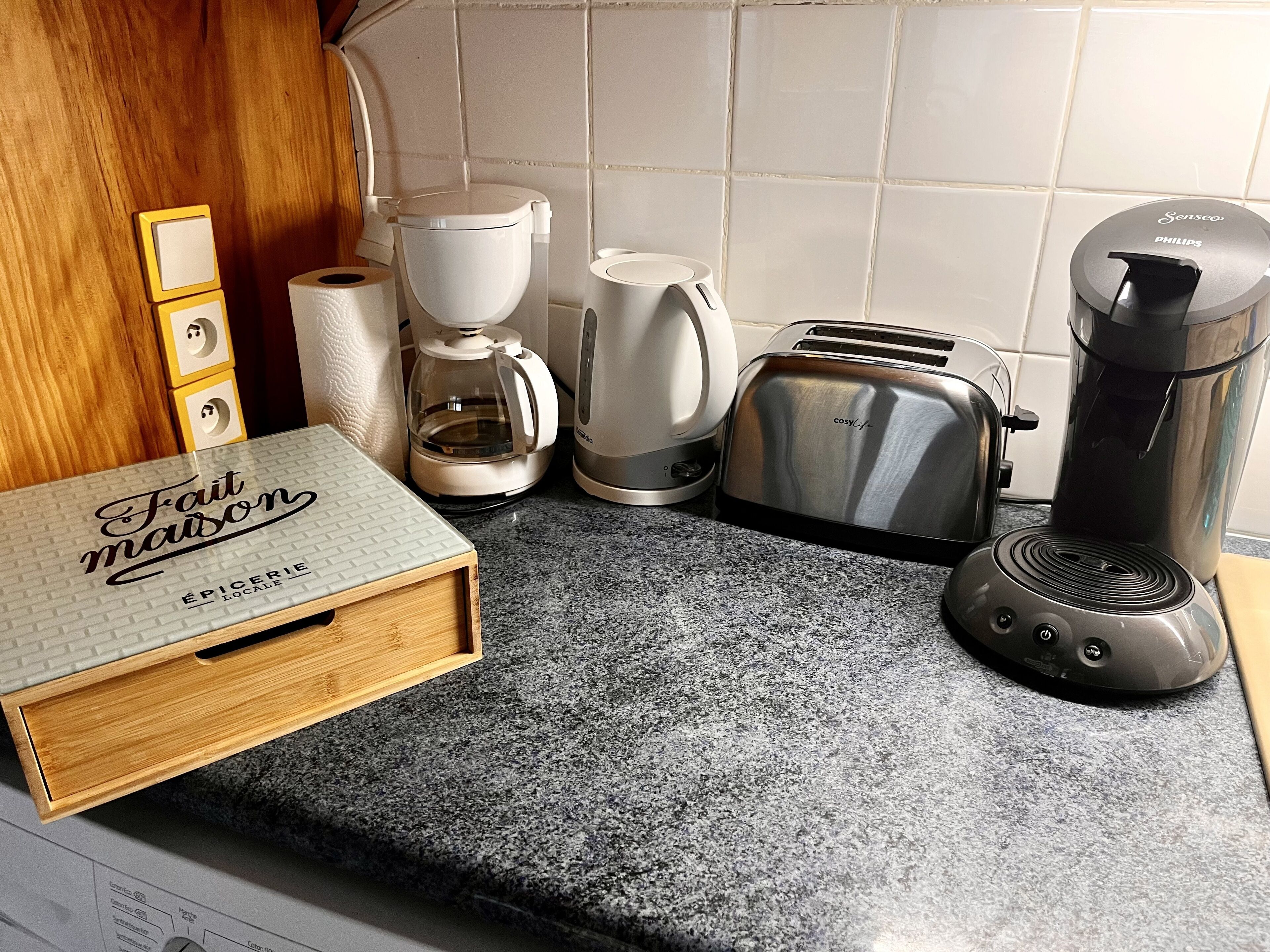 A kitchen counter with a coffee maker, toaster, and a box labeled "Fait maison".