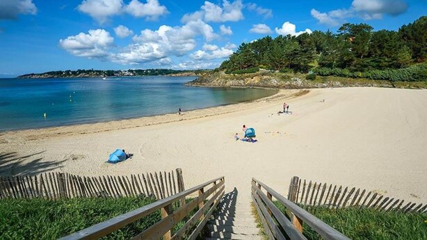 Una playa con un paseo de madera que conduce a la orilla, cielo azul despejado y mar tranquilo.