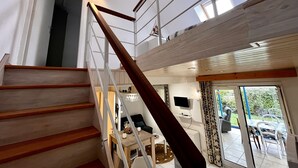 Una escalera conduce a un segundo piso con detalles de madera, un comedor con mesa y sillas, y un televisor montado en la pared.