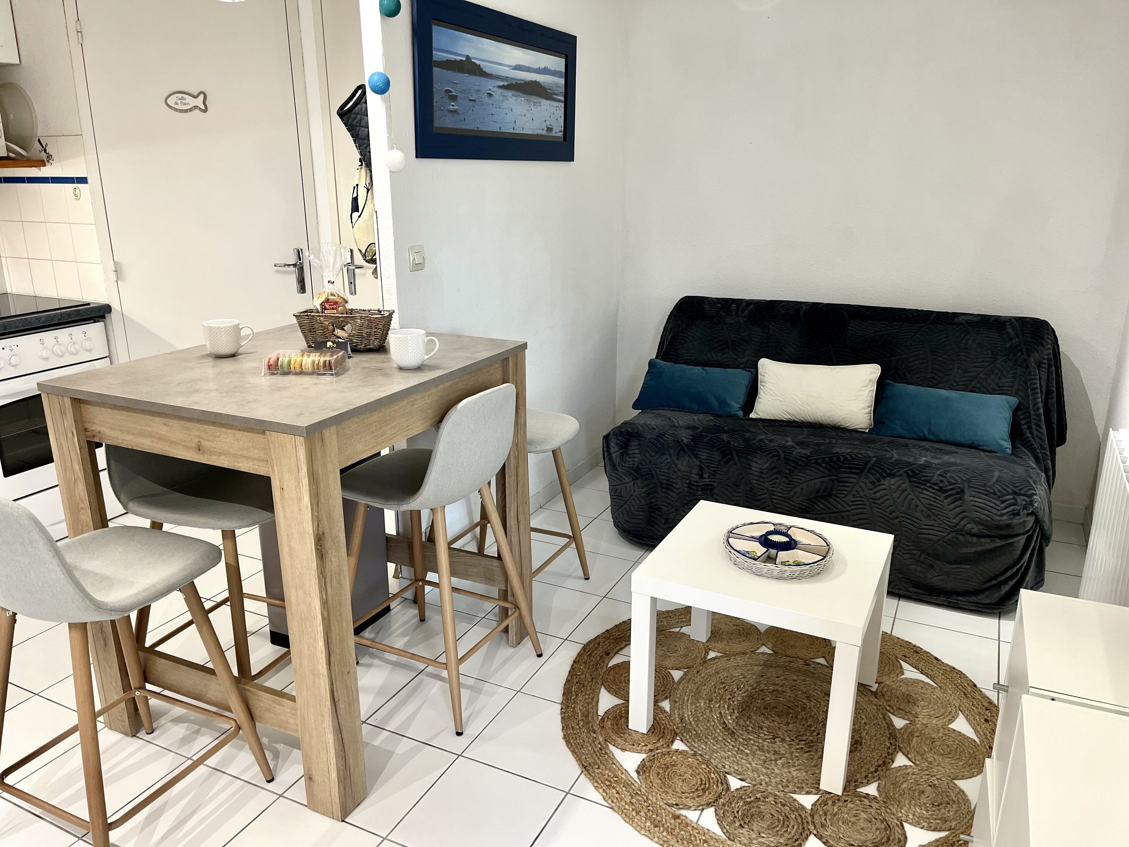 Een moderne keuken met witte kasten, een houten eettafel en een zwarte bank met blauwe kussens.