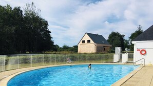 Una piscina con valla blanca, un flotador salvavidas y una casa al fondo.