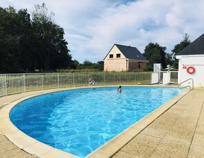 A swimming pool with a white fence, a lifebuoy, and a house in the background. - Keraven, charming cottage, shared pool (Moëlan-sur-Mer)