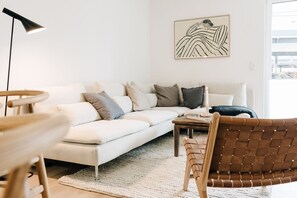 A living room with a white sofa, a wooden coffee table, a brown woven chair, and a black floor lamp.