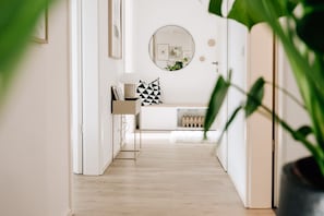 A hallway with a white wall, a round mirror, and a bench with geometric pillows.