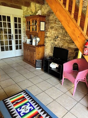 A living room with a stone wall, wooden staircase, a television, and a pink chair.