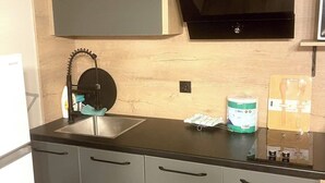 A modern kitchen with a black countertop, stainless steel cabinets, a built-in microwave, and a sink with a faucet. - Nesi apartment  (Pristina)