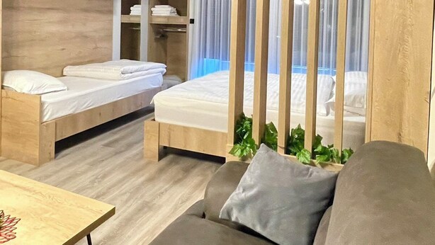 A modern hotel room with a wooden bunk bed, a sofa, a small table, and a window with curtains. - Nesi apartment  (Pristina)
