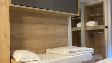 A bunk bed with a built-in TV and storage shelves, a shower area, and a wooden floor.