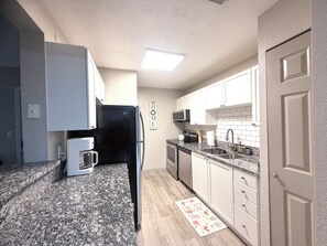 A compact kitchen with white cabinets, a black refrigerator, a microwave, and a coffee maker.