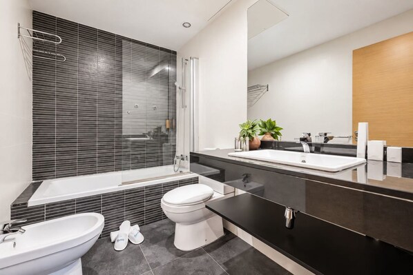 A modern bathroom with a bathtub, toilet, bidet, and a large mirror.
