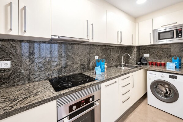 A modern kitchen with white cabinets, a black stove, a microwave, and a washing machine.