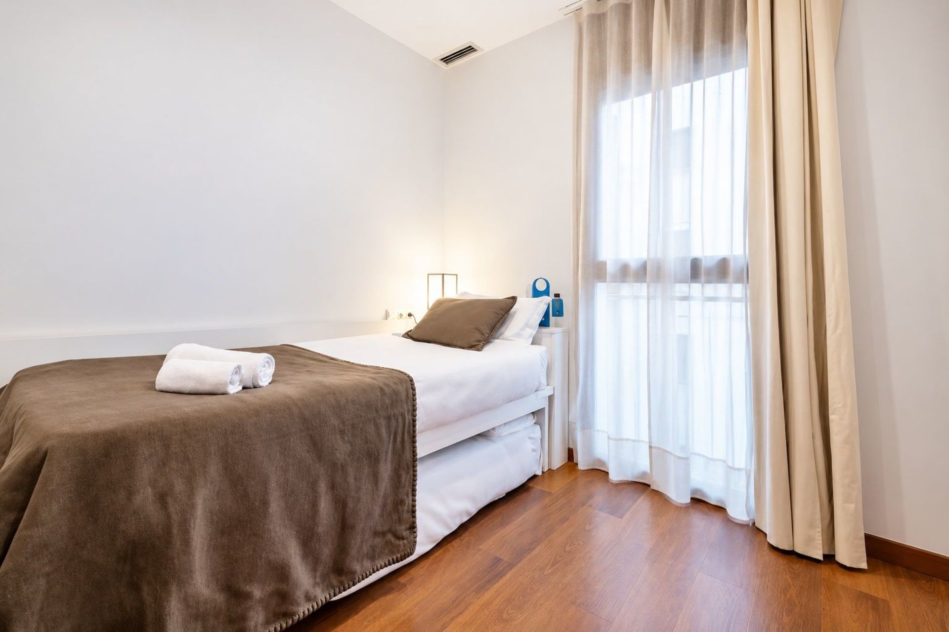 A hotel room with a single bed, a bedside table, a lamp, and a window with curtains.