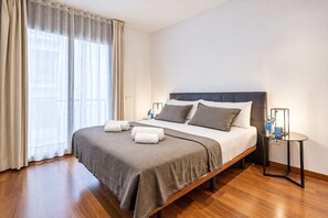 Ein Hotelzimmer mit Bett, Nachttisch, Lampe und einem Fenster mit Vorhängen.