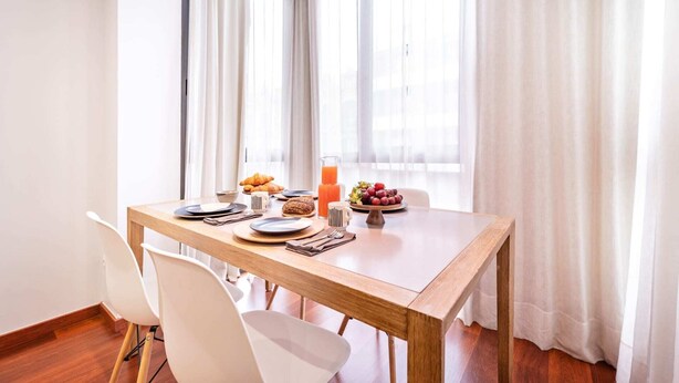 A dining area with a wooden table set for breakfast, including croissants, fruit, and juice. - Sweett | Eixample 4D (Barcelona)