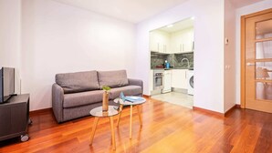 A modern living room with a grey sofa, a small round table with a laptop, and a TV on a stand. - Sweett | Eixample 4D (Barcelona)