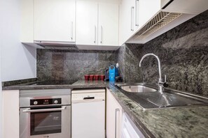 Una cocina compacta con armarios blancos, un lavamanos de acero inoxidable, horno empotrado y lavavajillas.