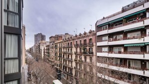 Fila de edifícios residenciais com varandas, uma rua estreita com veículos estacionados e um edifício alto ao fundo.
