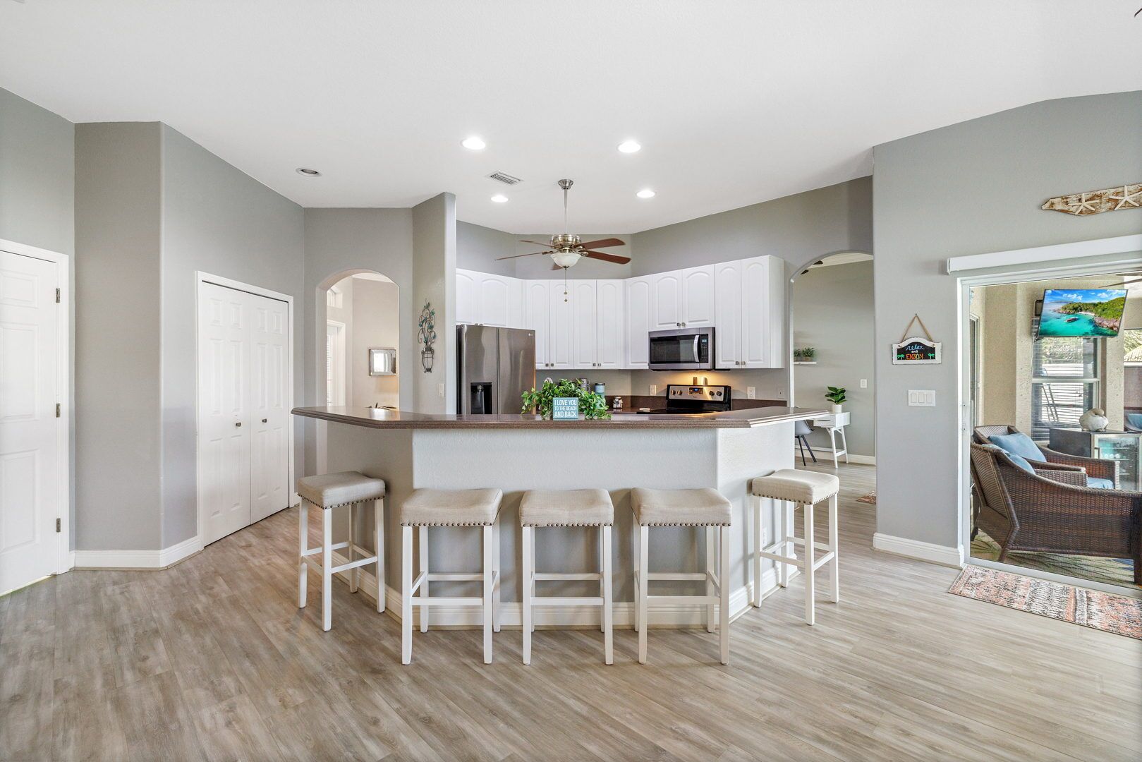 A modern kitchen with a central island, bar stools, and a dining area with wicker furniture.
