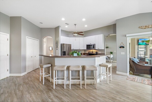 A modern kitchen with a central island, bar stools, and a dining area with wicker furniture.