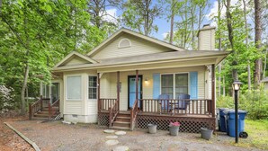 Une maison à deux étages avec un porche, des marches menant à l’entrée et un espace abrité avec des chaises.