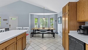 Une cuisine avec un plan de travail blanc, des meubles de rangement en bois, une table à manger avec des chaises et un lave-vaisselle.