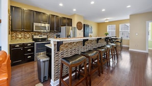 A modern kitchen with dark cabinets, a brick backsplash, and a bar area with stools. - Seaside Village 4 by Seaside Vacations & Sales (Ocean City)