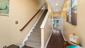 A hallway with a carpeted staircase, a bench, and a wall clock. - Seaside Village 4 by Seaside Vacations & Sales (Ocean City)