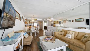 Ett vardagsrum med en beige soffa, ett vitt soffbord och en matplats med ett vitt bord och stolar.
