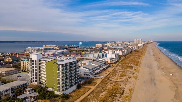 Un paisaje urbano costero con una extensa playa, edificios modernos y una torre de agua destacada.