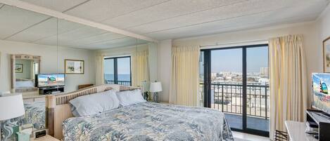 Ein Hotelzimmer mit einem großen Bett, einem Fernseher, einem Schreibtisch und einem Balkon mit Blick auf die Stadt.