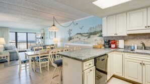 Una cocina con gabinetes blancos, encimera de granito y un mural que representa una escena de playa.