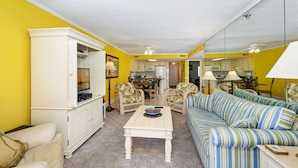 A compact living space with a sofa, a coffee table, and a cabinet. A dining area is visible in the background. - Summer Beach 807 by Seaside Vacations & Sales (Ocean City)
