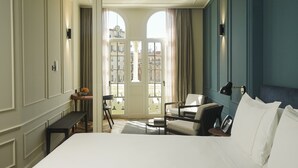A hotel room with a large bed, a desk with a chair, a sofa, and a view of the city through a glass door. - Mercer Plaza Sevilla 5 GL (Seville)