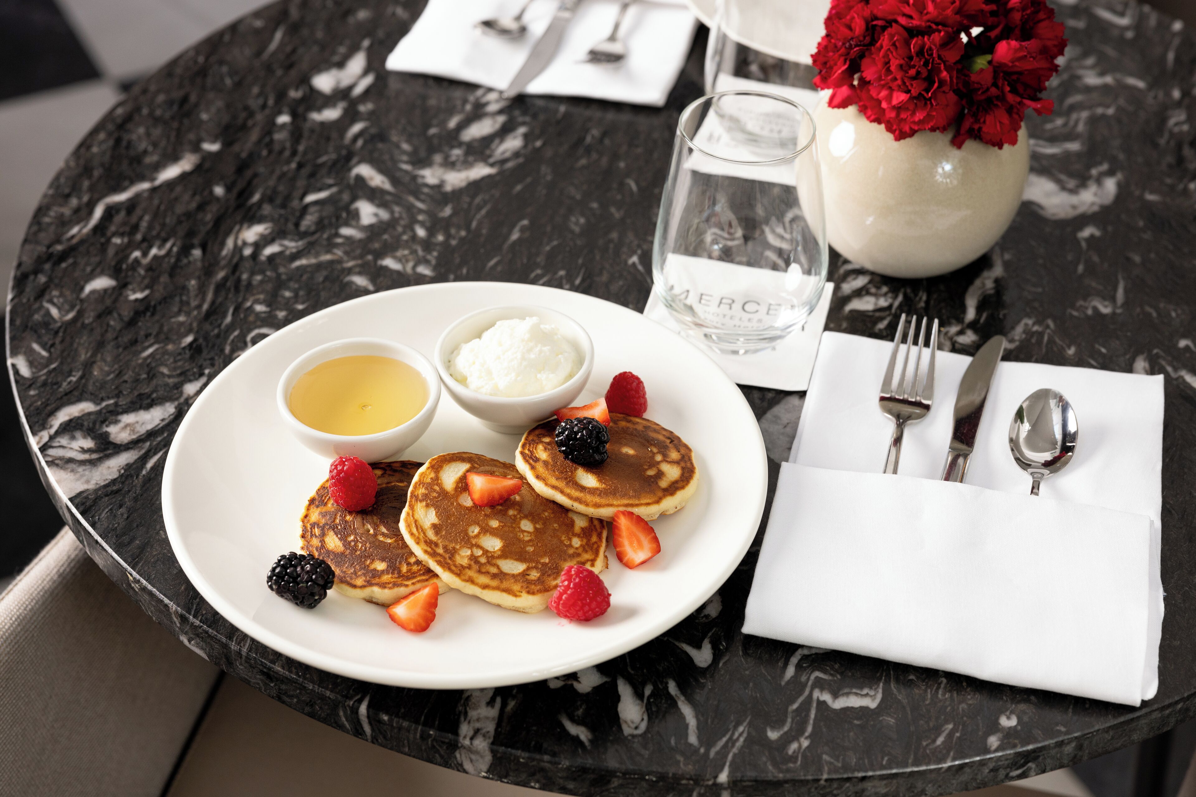 A breakfast setting with pancakes, berries, and two small bowls of cream on a marble table.