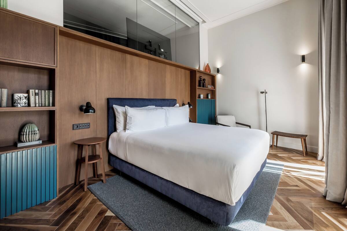 A modern bedroom with a large bed, wooden shelving, a small side table, and a floor lamp.