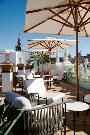 Terraço no telhado com área de estar ao ar livre, guarda-sóis e vista para edifícios históricos.