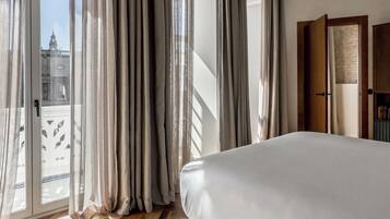 Ein Schlafzimmer mit einem großen Bett, einer Glastür, die auf einen Balkon führt, und einer Holztür rechts.