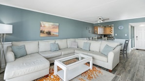 A living room with a sectional sofa, a coffee table, and a painting of a beach scene. - Wight Bay 559 by Seaside Vacations & Sales (Ocean City)