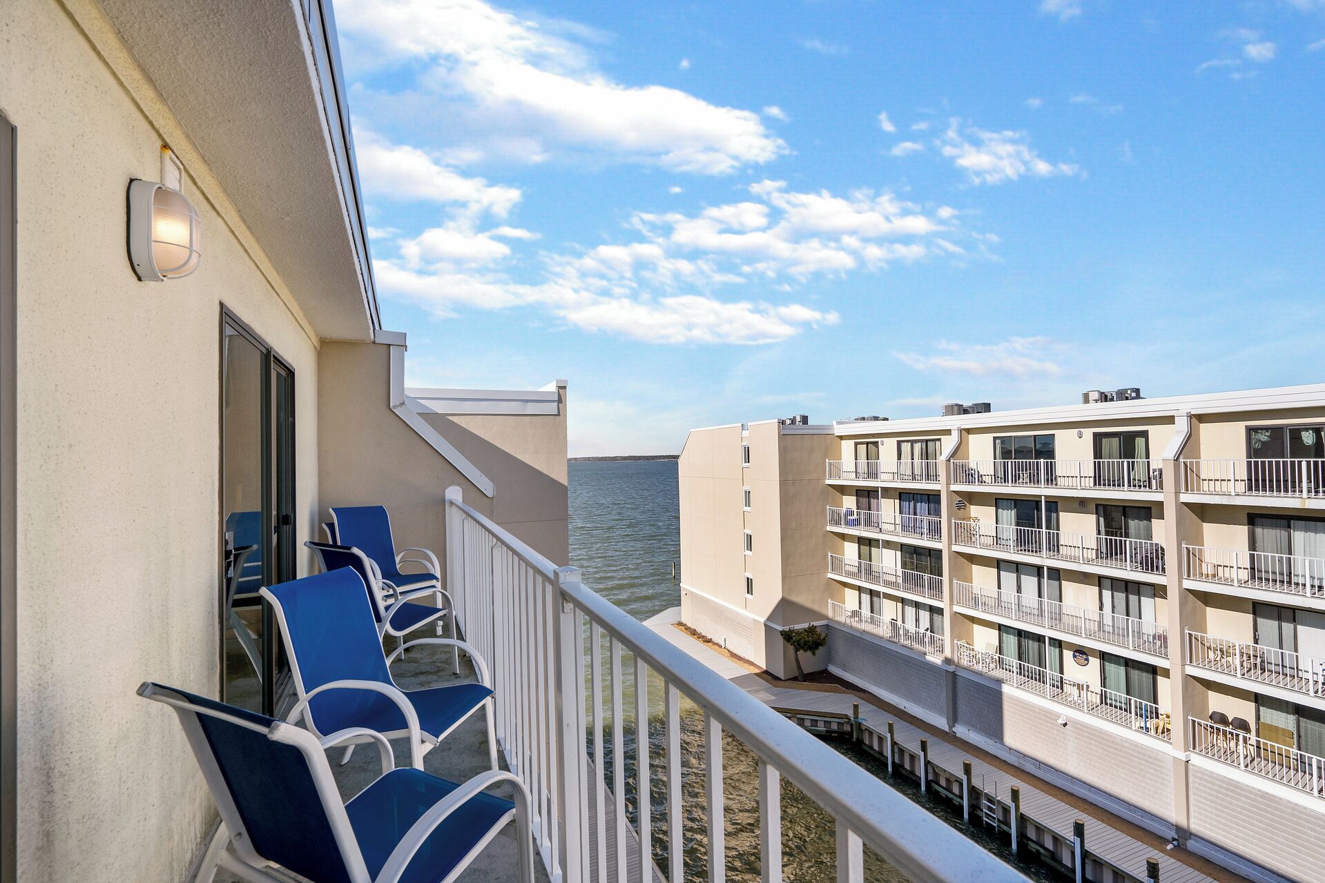 Un balcon avec des chaises bleues, une balustrade blanche et une vue sur un bâtiment situé de l’autre côté de l’eau.
