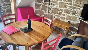 A cozy dining area with a round wooden table, pink chairs, and a stone wall backdrop. - Gite Daim, Gite en Pleine Nature (Avène)