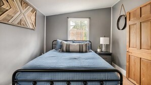 A bedroom with a bed, a nightstand, a lamp, a window, and a door. - Creekside Cabin w Hot Tub, Fire Pit, Deck & Grill! (Mount Jackson)