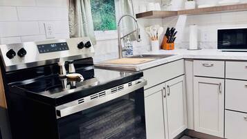 Una cocina moderna con estufa de acero inoxidable, armarios blancos, un microondas y un ventanal con cortinas.