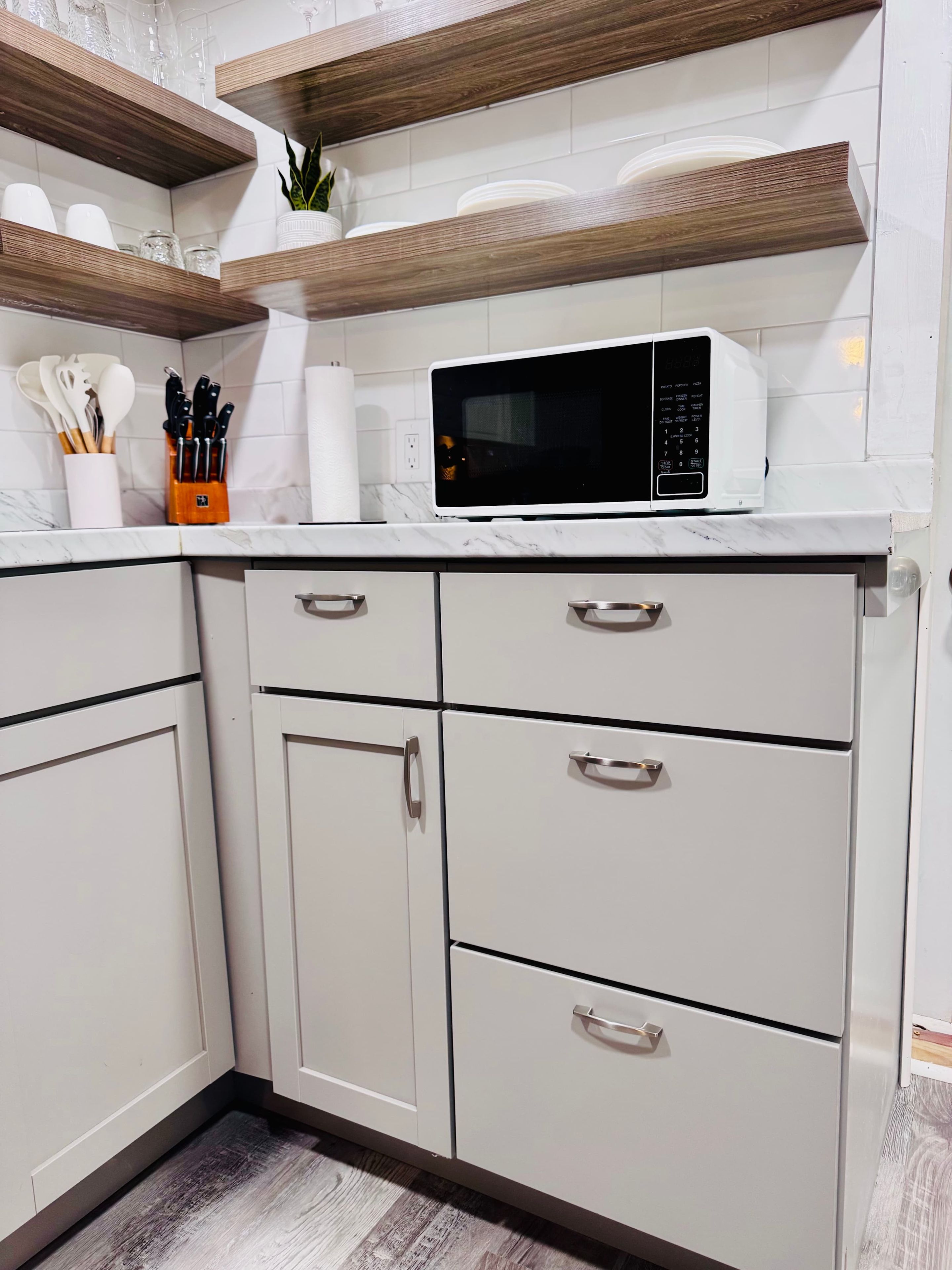 A kitchen with white cabinets, a microwave, and wooden shelves.