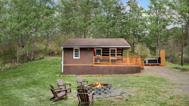 A cabin with a deck, a fire pit, and two Adirondack chairs. - Creekside Cabin w Hot Tub, Fire Pit, Deck & Grill! (Mount Jackson)