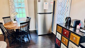 A compact kitchen with a stainless steel refrigerator, a wooden dining table with chairs, and a cabinet with multiple drawers.