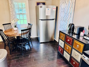 A compact kitchen with a stainless steel refrigerator, a wooden dining table with chairs, and a cabinet with multiple drawers. - Creekside Cabin w Hot Tub, Fire Pit, Deck & Grill! (Mount Jackson)