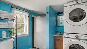 A compact bathroom with a shower, a toilet, and two stacked washing machines. - Creekside Cabin w Hot Tub, Fire Pit, Deck & Grill! (Mount Jackson)