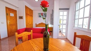 A room with a wooden table, a red sofa, a wooden door, and a window. - Apartamento Estudio Mirador de los Poetas (Puerto de las Nieves)