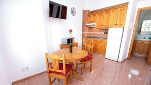 A dining area with a wooden table and chairs, a small side table with a vase, and a kitchen with wooden cabinets and a refrigerator. - Apartamento Estudio Mirador de los Poetas (Puerto de las Nieves)