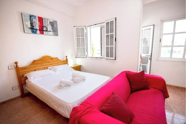 A bedroom with a wooden bed, a red sofa, and a painting on the wall. - Apartamento Estudio Mirador de los Poetas (Puerto de las Nieves)